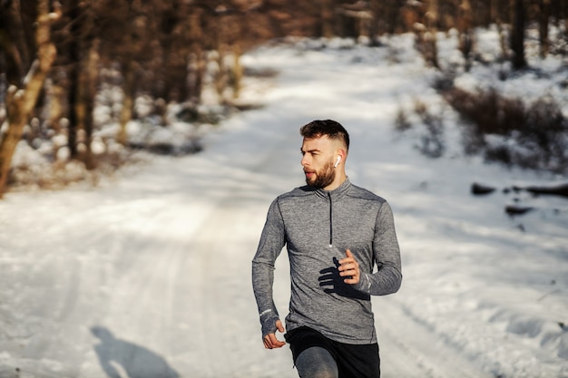 Fit sportman die in het bos loopt op een zonnige besneeuwde winterdag. Buitenfitness, cardio-oefeningen, winterfitness