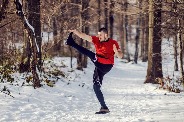 Foto fit sportman die opwarmingsoefeningen doet terwijl hij in de natuur op een besneeuwd pad staat in de winter. gezonde gewoontes, wintersport