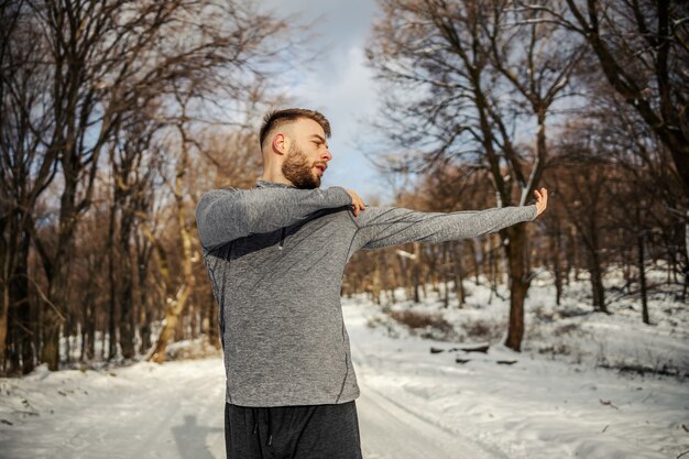 Fit sportman die opwarmingsoefeningen doet terwijl hij in de natuur staat op een besneeuwde winterdag. Winterfitness, gezonde levensstijl