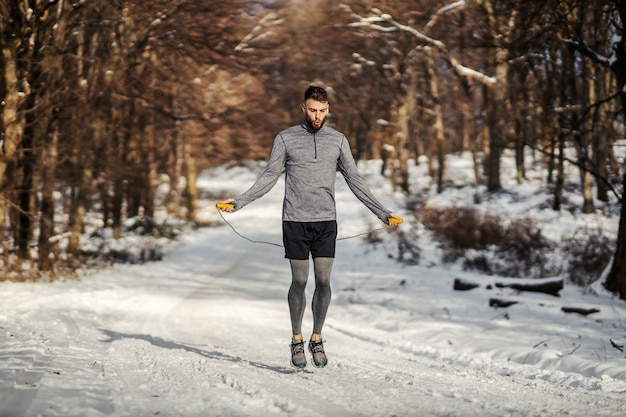 Fit sportman touwtjespringen in bos op besneeuwde winterdag. Winterfitness, cardio-oefeningen