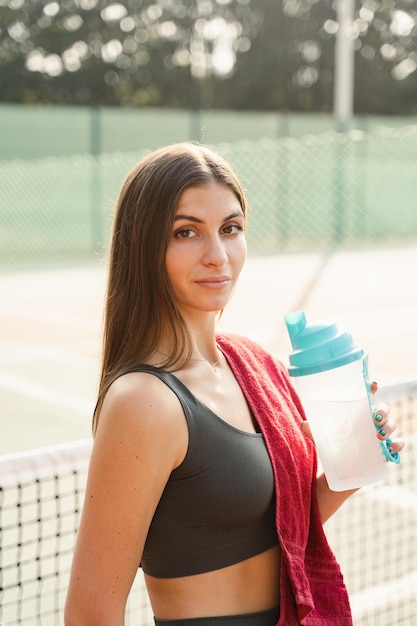 Photo fit sports model is resting after training and drinking water from a bottle sports lifestyle beautiful girl posing on the tennis court