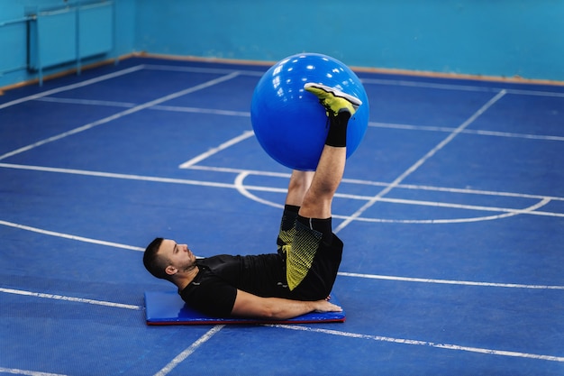 Fit sportsman in excellent shape doing Crunches with pilates ball in sport hall.