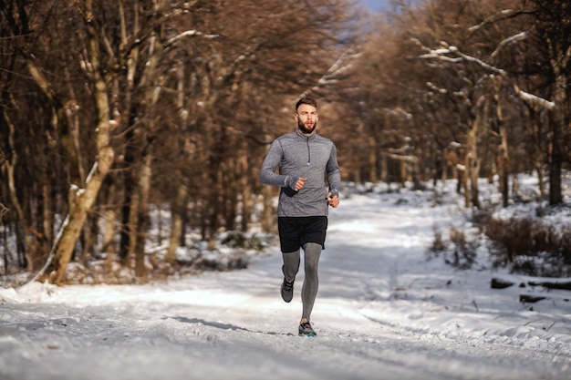 Fit sportsman running in forest at sunny snowy winter day. Outdoor fitness, cardio exercises, winter fitness