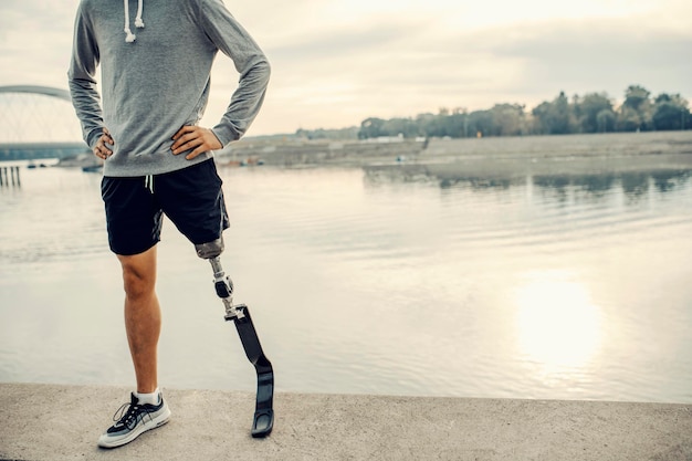 Photo a fit sportsman with prosthetic leg standing at the quay with hands on hips proud handicapped man