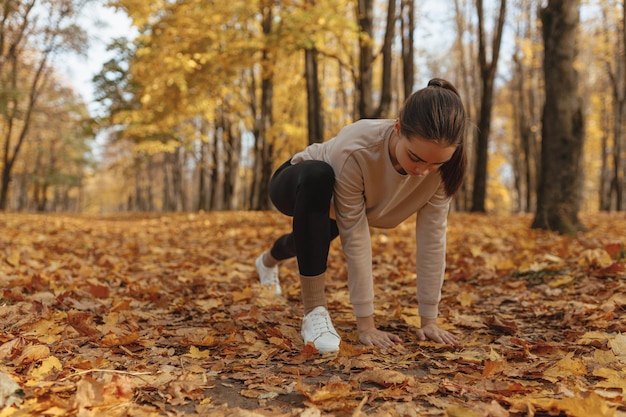 Fit sportswoman doing lunge exercise and stretching legs during fitness workout in autumn park