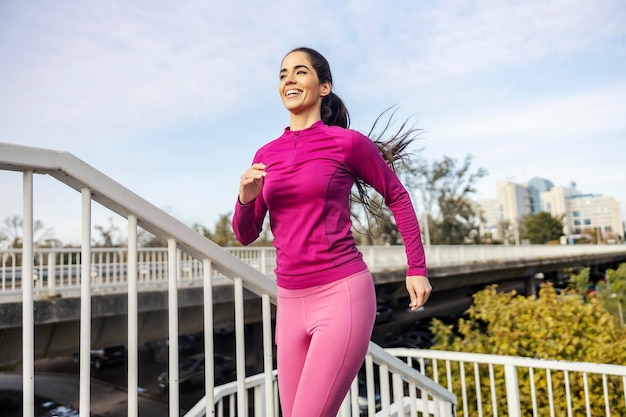 A fit sportswoman is running on the bridge on city street