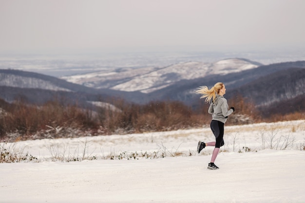 写真 冬の自然の中で雪の中でジョギングするスポーツウーマンに合います。健康的なライフスタイル、有酸素運動、冬のフィットネス