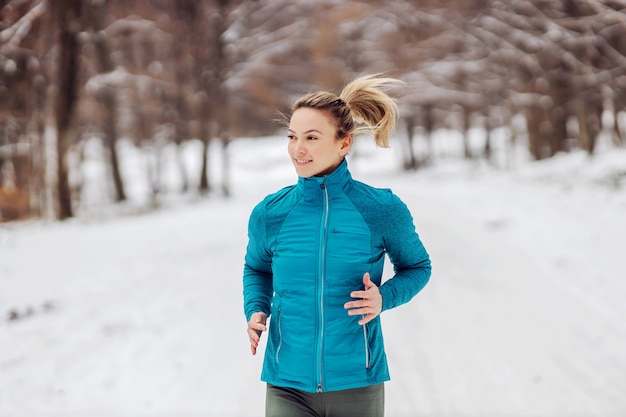 Fit sportswoman running in nature on a snowy path. Cold weather, snow, healthy life, fitness