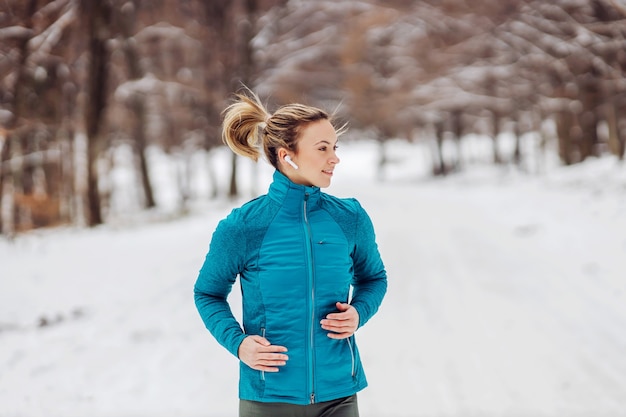 Fit sportswoman running in nature on a snowy path. Cold weather, snow, healthy life, fitness