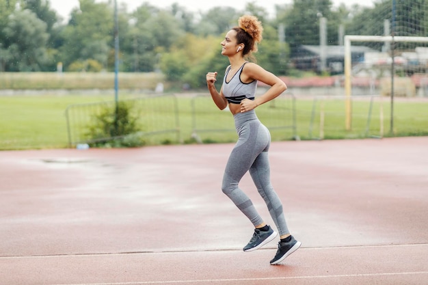 A fit sportswoman with healthy habits is listening to music and running on a rainy day in a stadium