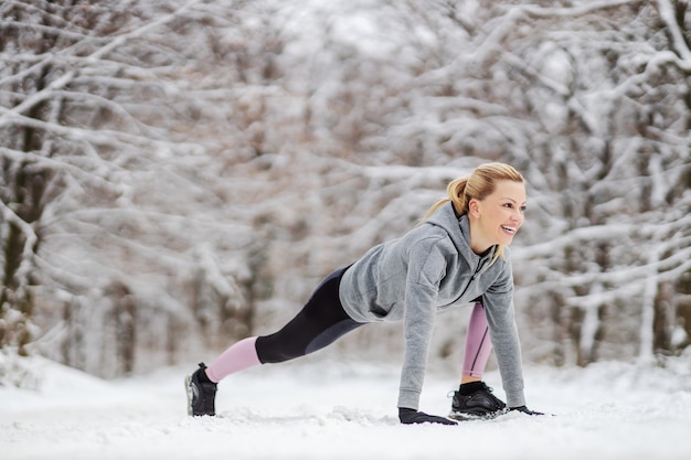 Fit sportvrouw in sportkleding warming-up en rekoefeningen doen in bos op besneeuwde pad in de winter. Gezonde gewoontes, winterfitness
