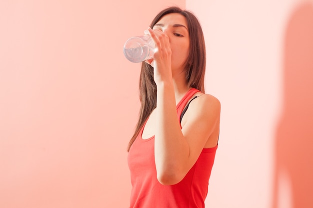 Fit sporty girl in fitness clothes drinking water during training