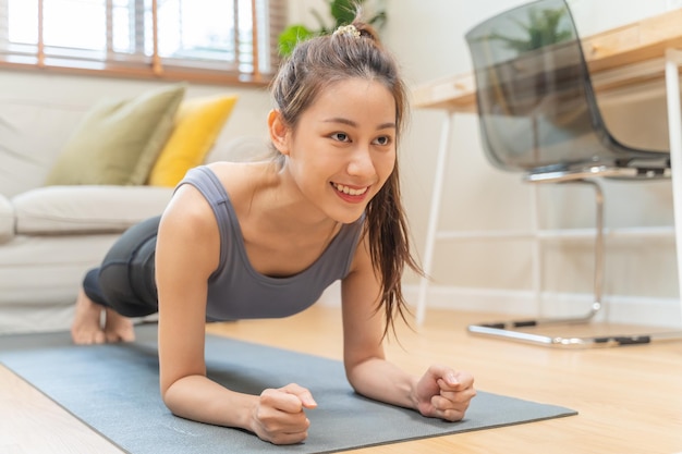 요가를 하는 스포티한 아시아 젊고 아름다운 여성 소녀는 플랭크와 신체 훈련을 하고 거실에서 매트 위에서 강한 연습을 하고 집에서 평상복을 입은 운동 피트니스 운동 사람들