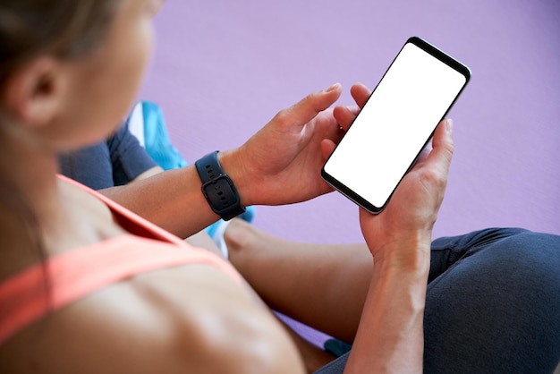 Foto fit donna sportiva che tiene il telefono simulando lo schermo bianco utilizzando l'app fitness yoga