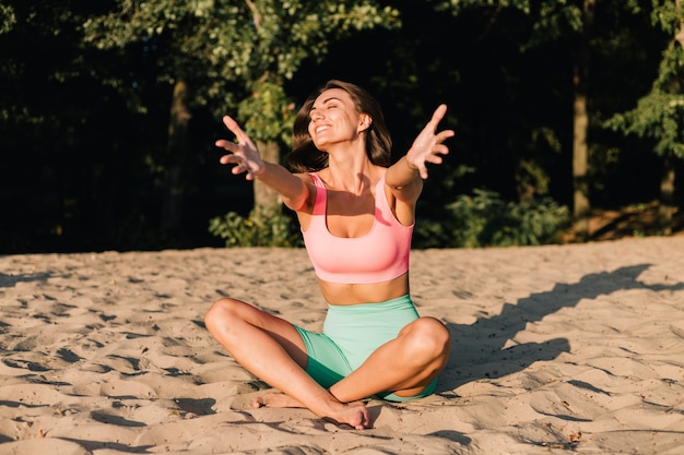 Подходящая спортивная женщина в идеальной форме на закате на пляже в спокойной позе йоги