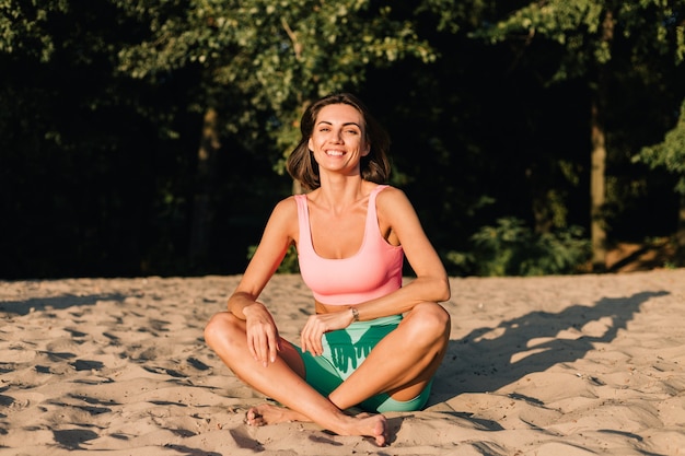 Подходящая спортивная женщина в идеальной форме на закате на пляже в спокойной позе йоги