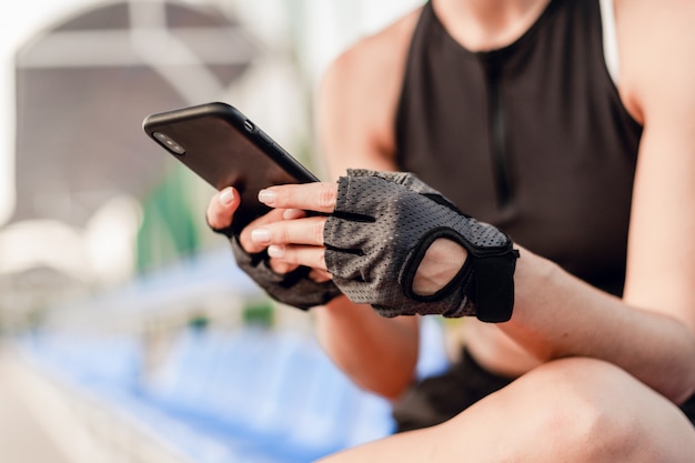 Photo fit sporty woman uses phone on the stadium in the morning during fitness workout