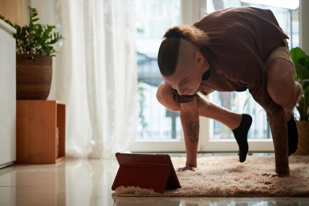 タブレットコンピュータの画面でチュートリアルに従うときに逆立ちを練習している強い若い男にフィットします