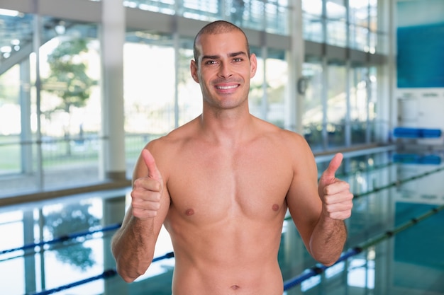 Fit swimmer gesturing thumbs up by pool at leisure center