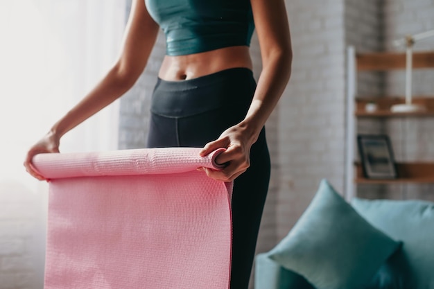 Fit unrecognised woman folding exercise mat after working out\
at home equipment for fitness pilates