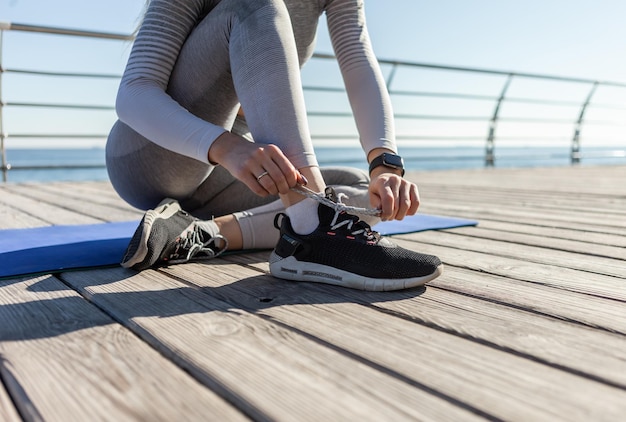 Fit vrouw die schoenveters bindt terwijl ze op een mat op het strand zit op een zonnige dag Gezonde levensstijl