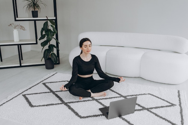 Fit vrouw die yoga doet en online tutorials bekijkt over laptoptraining in de woonkamer