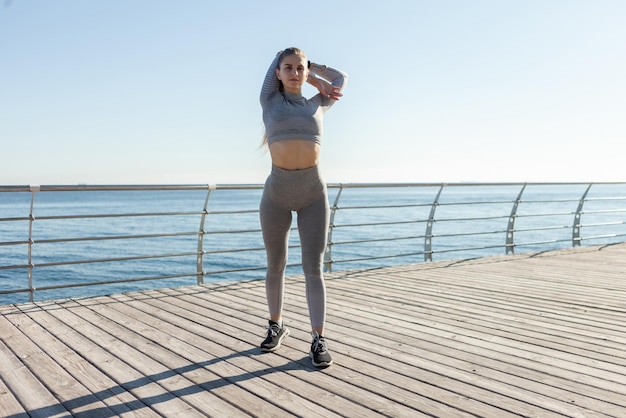 Fit vrouw in sportkleding die zich uitstrekt op het strand op een zonnige dag Gezonde levensstijl