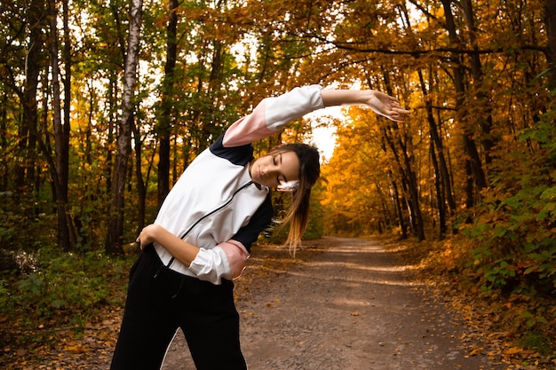 Fit vrouw in sportkleding doet zijwaartse bochten buiten in de herfst. Fitness, actieve ochtend, training en gezonde levensstijl. Park of bos op de achtergrond. Opwarmen voor de training.
