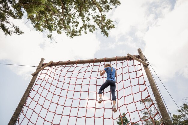 Fit vrouw klimmen over het net tijdens hindernissenparcours in bootcamp