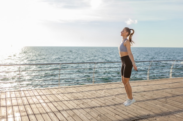 Fit vrouw springtouw op het strand bij zonsopgang