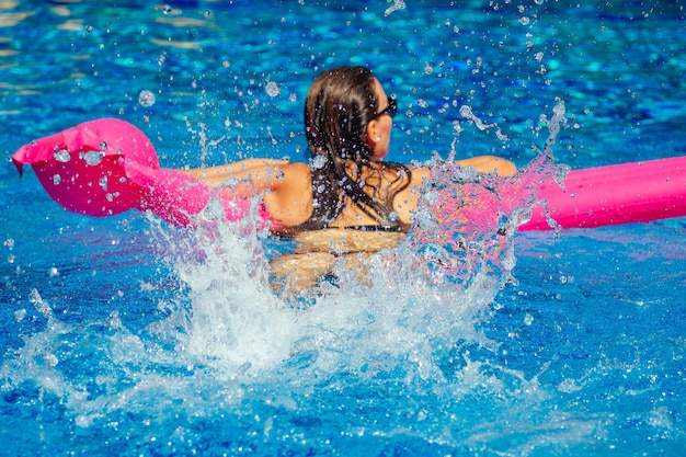 Fit vrouw uit te werken in het zwembad. jong mooi meisje doet aquagym oefening drijvend op een opblaasbare roze matras splash waternevel.