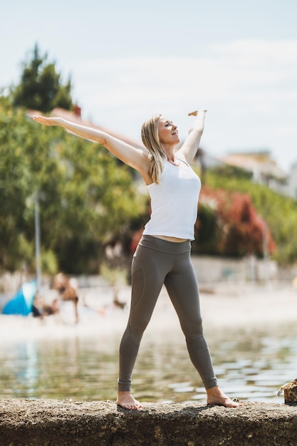 Fit vrouw van middelbare leeftijd ontspannen en genieten van de zomerdag voordat ze gaat trainen in de buurt van het zeestrand.