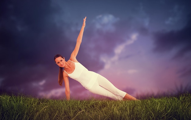 Montare la donna facendo esercizi di pilato nello studio fitness contro il cielo blu sopra l'erba