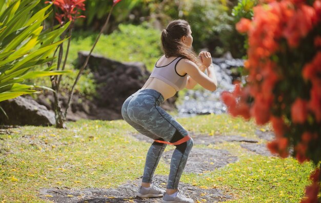 Fit woman doing squats on nature fitness girl doing squats with resistance band outdoor sporty girl