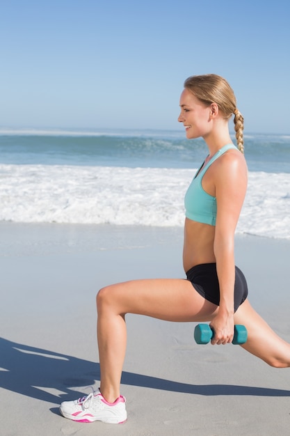 Fit woman doing weighted lunges on the beach