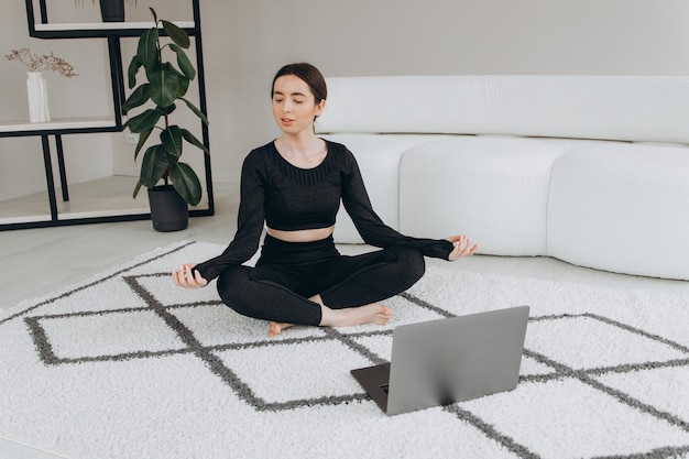 Fit woman doing yoga and watching online tutorials on laptop training in living room