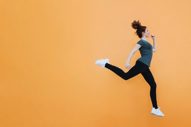 Fit woman jumping at orange wall