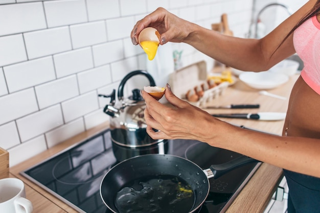 Fit woman in kitchen cracking egg into frying pan