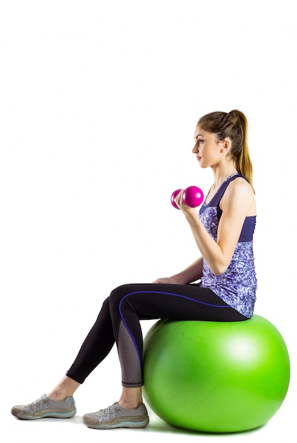 Fit woman lifting dumbbell sitting on ball