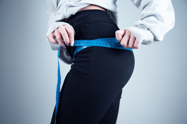 Fit woman measuring her waist on dark background