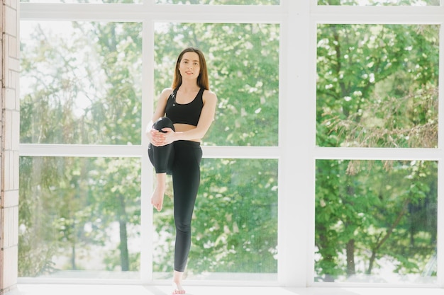 Fit woman pose yoga exercising in studio over panoramic window