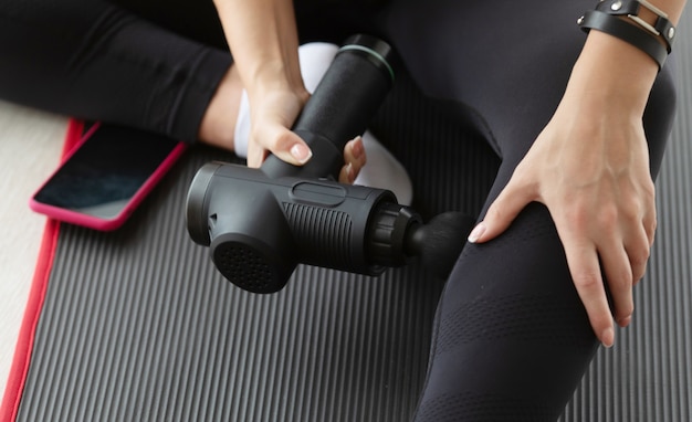 fit woman practicing selfmassage technique for buttocks applying therapeutic percussive massage gun