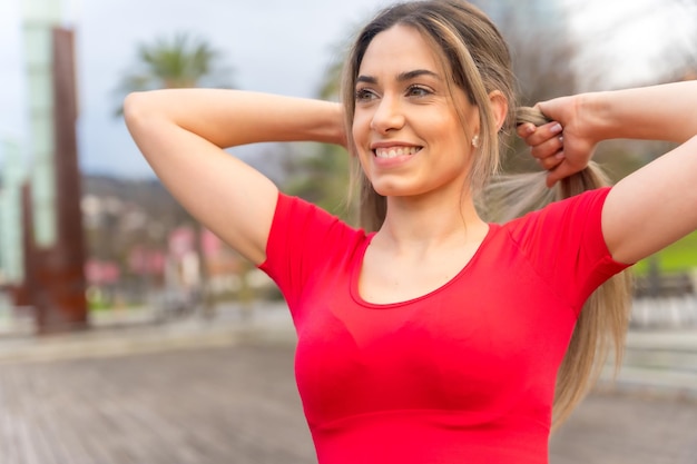 Подтянутая женщина в красной одежде занимается спортом в городе весной, надевает хвостик