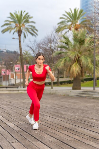 市内のフィットネス スポーツでヤシの木が茂る公園を走る赤い服を着たフィットの女性