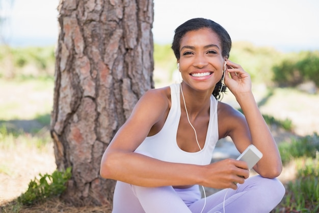 写真 音楽を聴いて木に座っている女性に合う