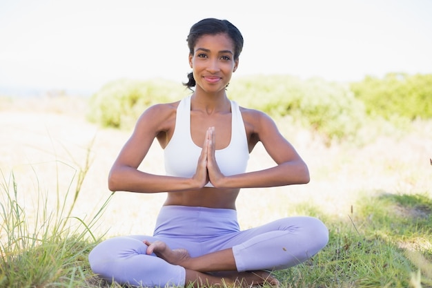 Fit woman sitting on grass in lotus pose smiling at camera