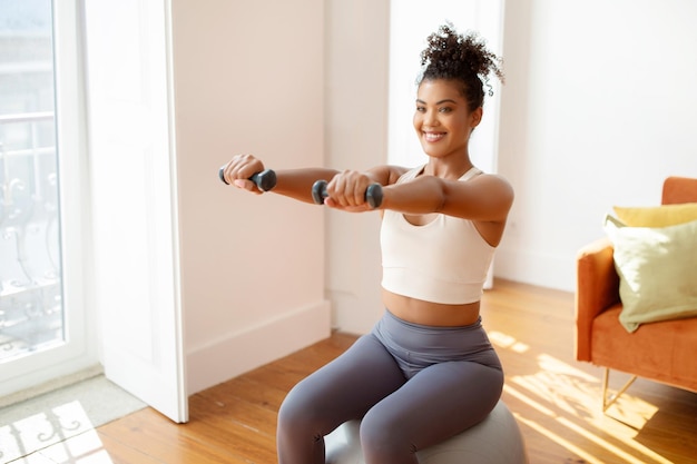 写真 バランスボールに座って体重を上げる体格の良い女性が室内運動をしています