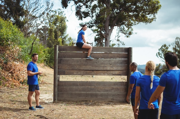 Fit woman sitting over wooden wall during obstacle course