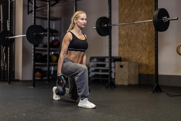 Foto donna in forma in abbigliamento sportivo che fa affondi con un kettlebell nelle sue mani in palestra allenamento funzionale