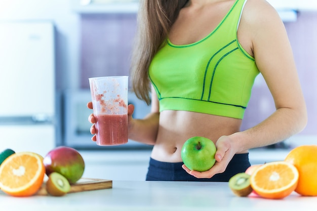 La donna adatta in abiti sportivi beve un frullato di frutta fresca per perdere peso. bevande dietetiche con vitamine per un'alimentazione sana